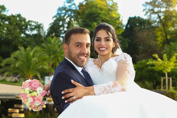 Le marié porte sa mariée dans un jardin, bouquet de roses à la main